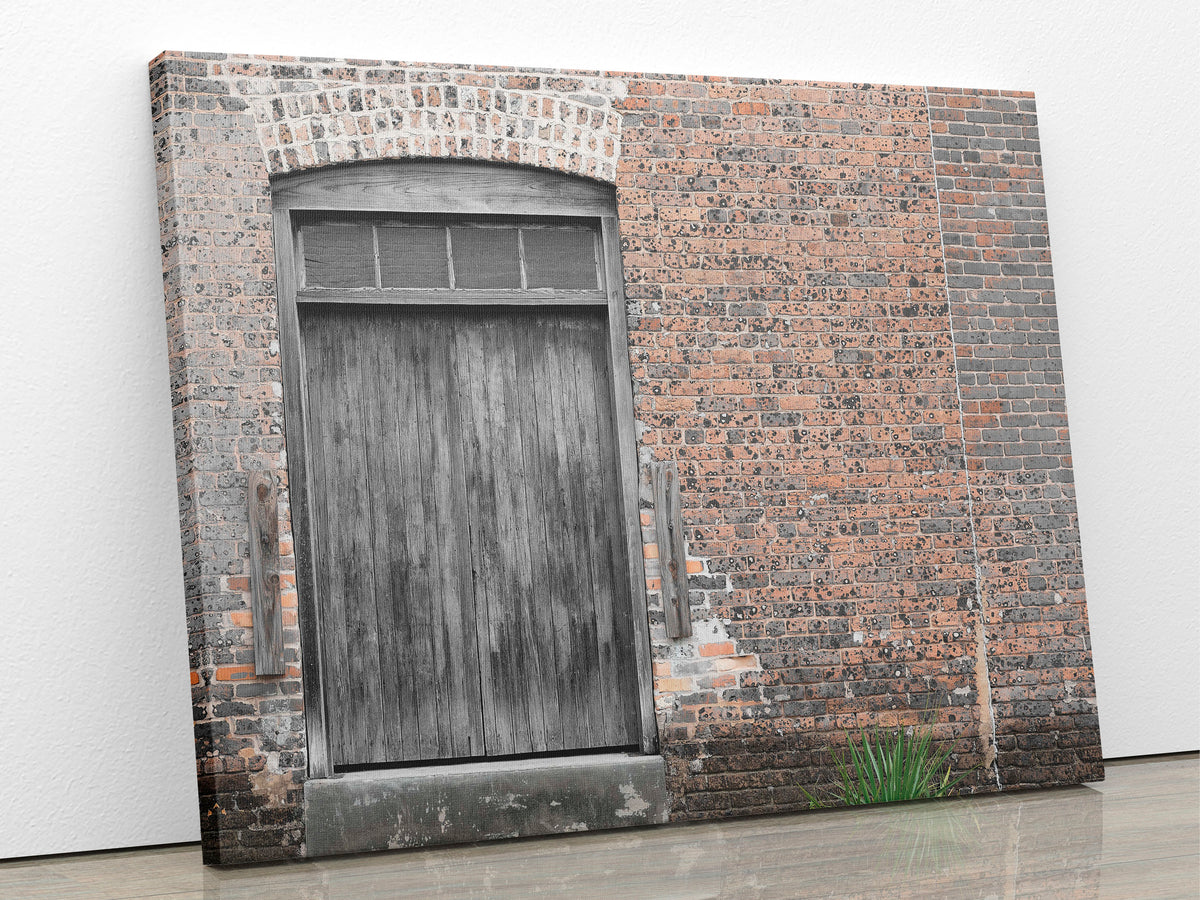 An image of wooden freight door and brick wall printed on 20x24 inch canvas wrapped on artist&#39;s stretcher bars. The cotton-poly canvas has a semi-gloss finish and is hand-stretched and stapled in place. Kraft paper covers the back of the frame.