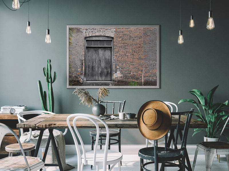 An image of wooden freight door and brick wall printed on 20x24 inch canvas wrapped on artist&#39;s stretcher bars. The cotton-poly canvas has a semi-gloss finish and is hand-stretched and stapled in place. Kraft paper covers the back of the frame.